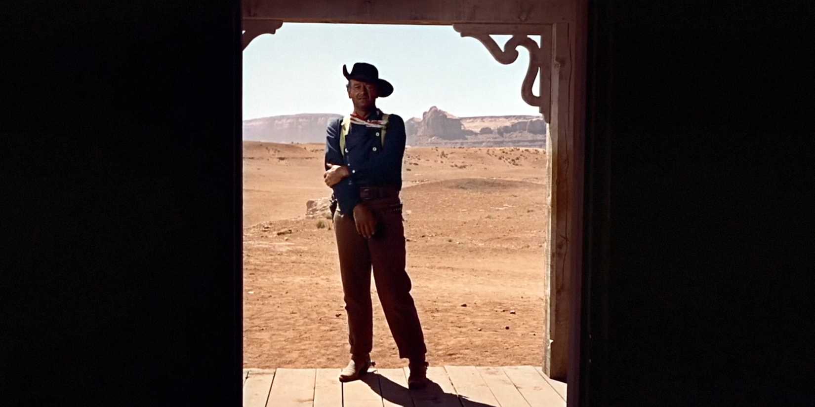 John Wayne as Ethan Edwards standing outside of a doorway in The Searchers.