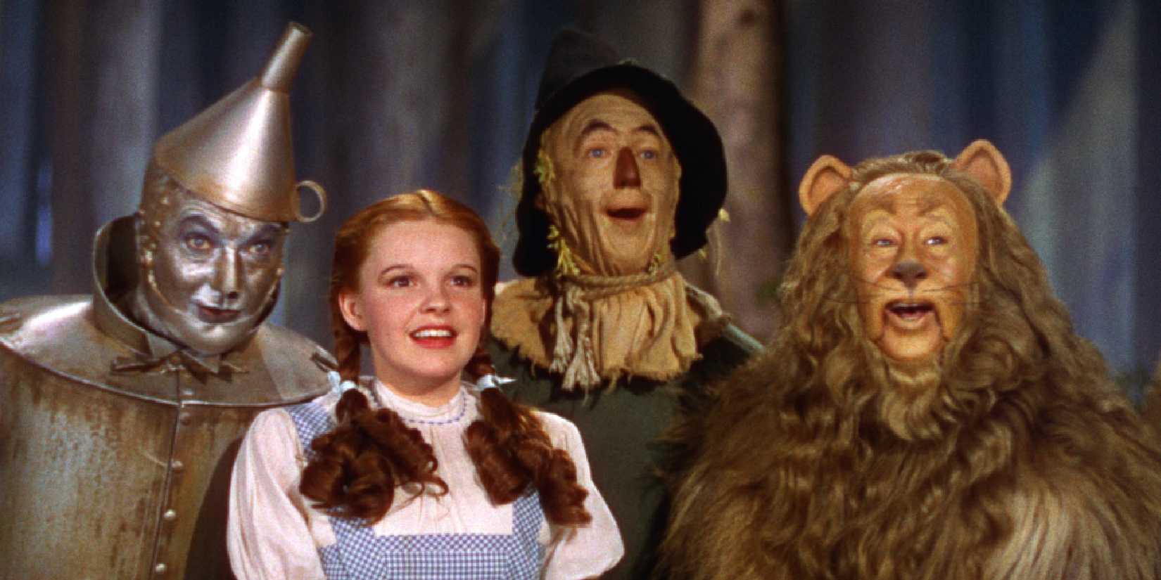 Dorothy, the Scarecrow, the Tin Man, and the Cowardly Lion look excited and smile in The Wizard of Oz.