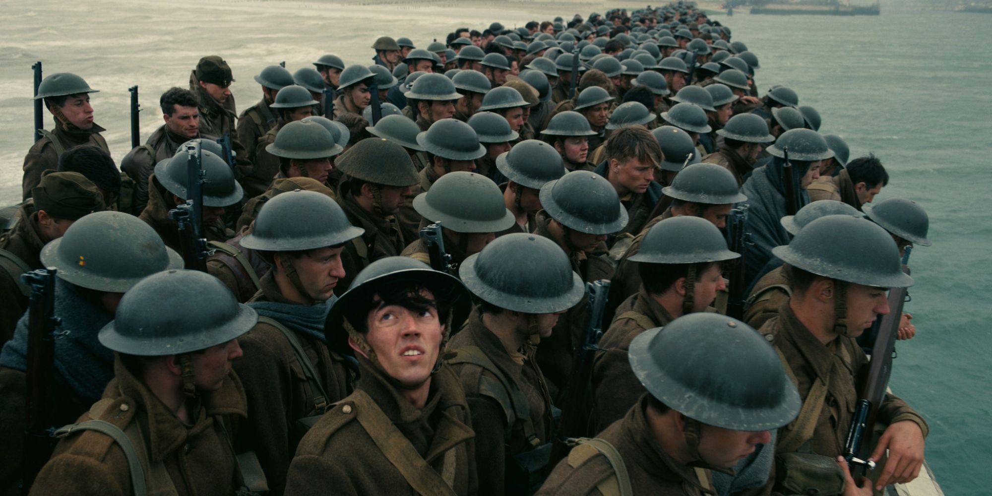 A group of soldiers wearing helmets packed tightly together on a shallow boat in water in Dunkirk. 