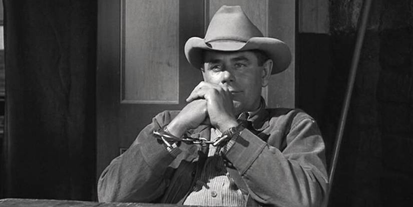 Glenn Ford sitting at a table in handcuffs in 3:10 to Yuma.
