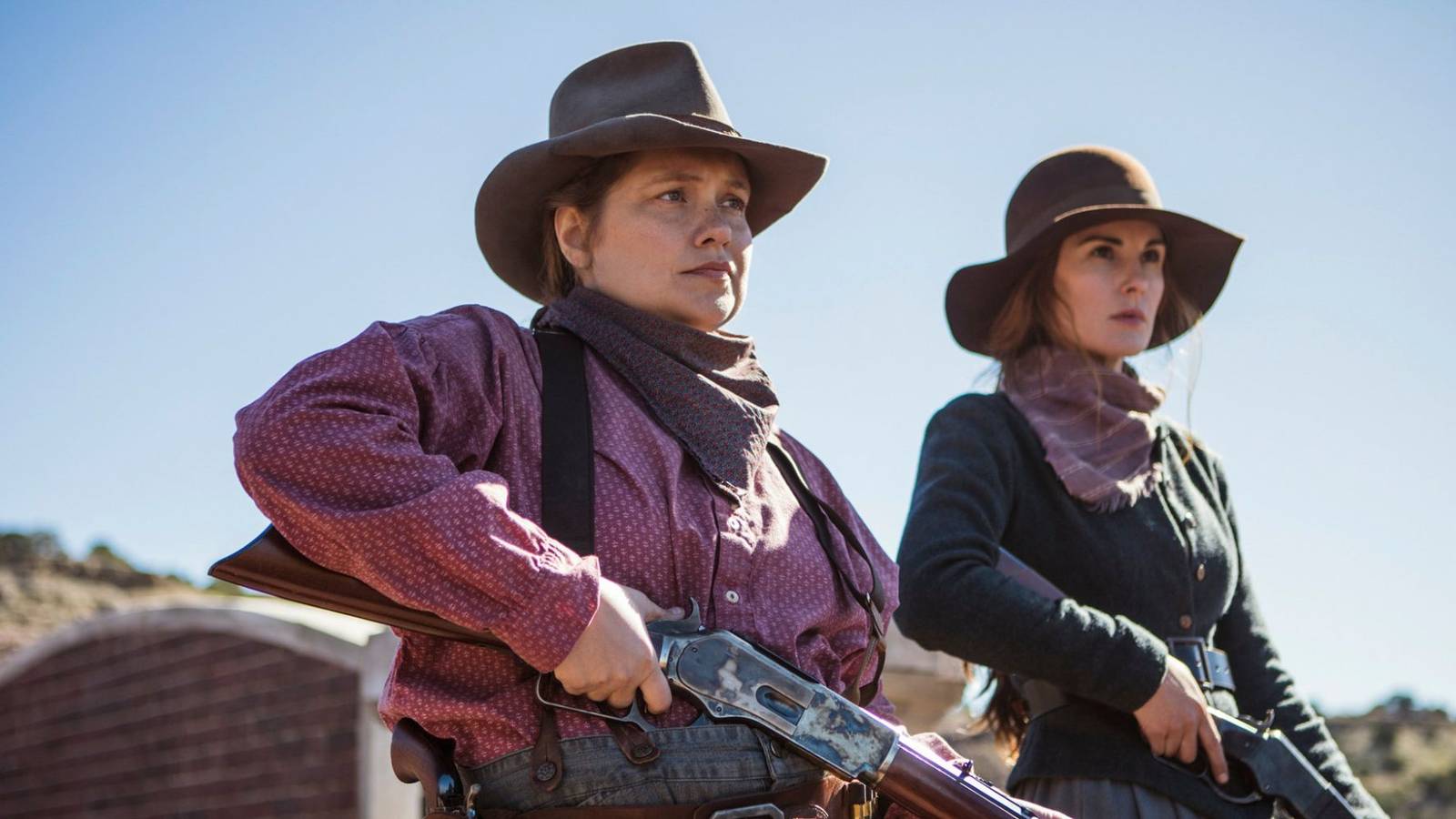 Two women in western apparel outdoors holding rifles and looking at something off-screen in Godless.