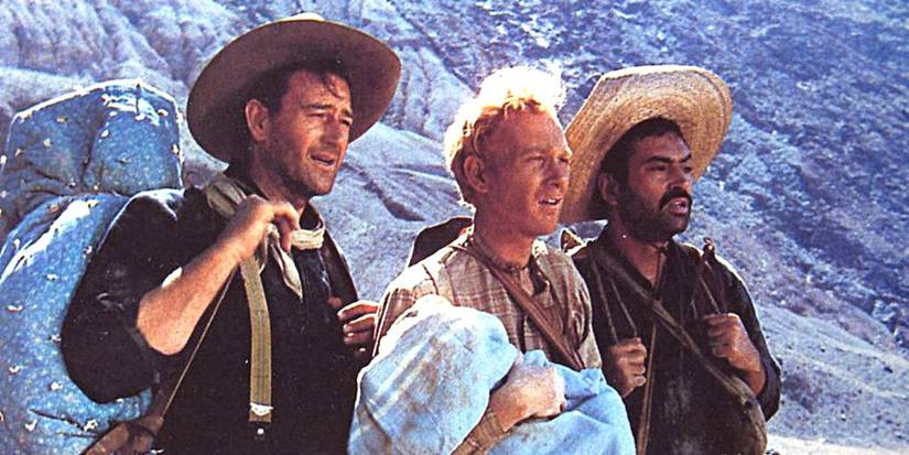 colorized still of John Wayne as Robert Hightower, Harry Carey Jr. as William Kearney holding a swaddled infant and Pedro Armendáriz as Pedro Roca Fuerte standing next to each other in a desert in 3 Godfathers (1948)