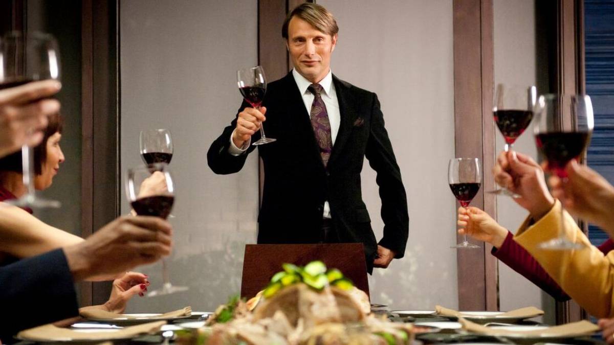 Mads Mikkelsen holding up a glass of wine with others in Hannibal
