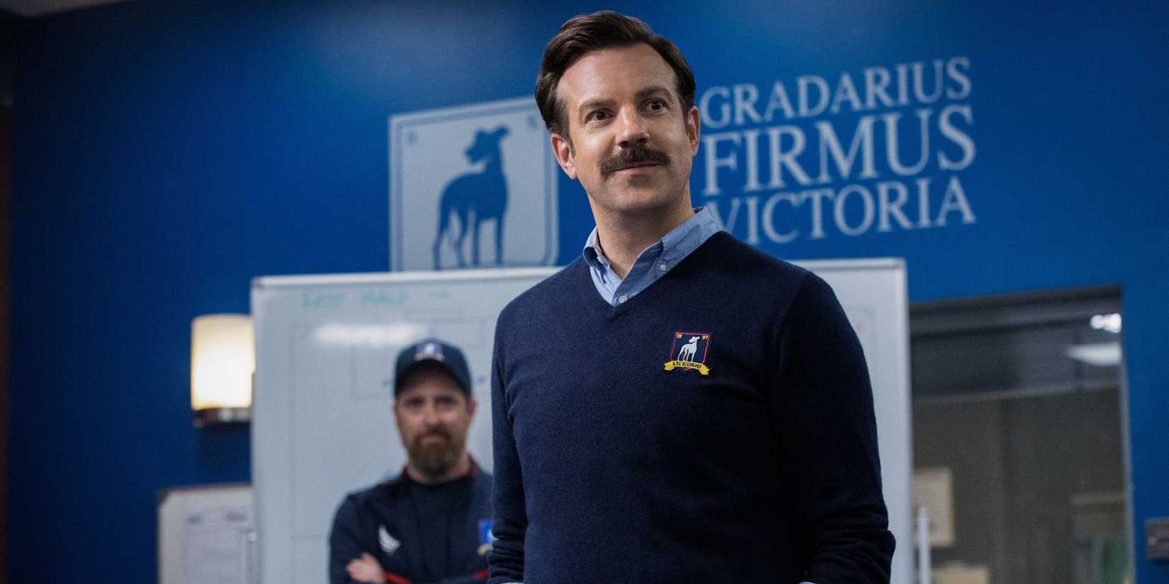 Jason Sudeikis as Ted Lasso with brendan Hunt as Coach Beard in the background in Ted Lasso.