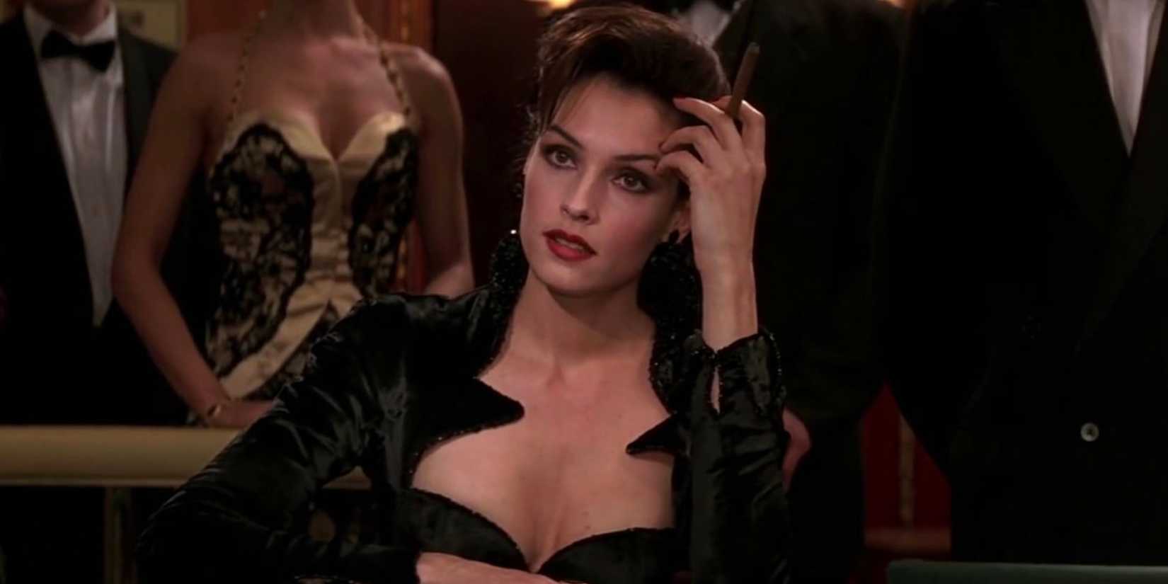 Ruthless assassin Xenia Onatopp (Famke Janssen) sits at a table while holding a cigar in 'GoldenEye'.