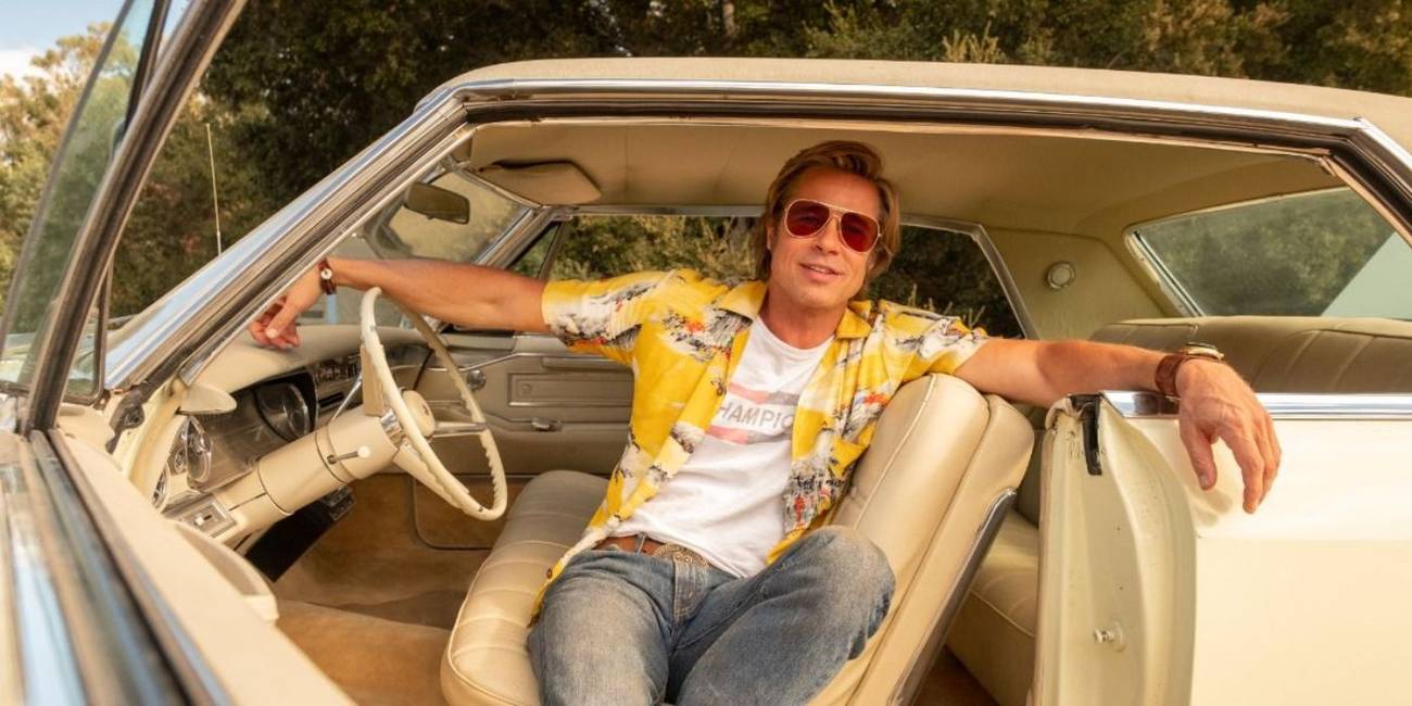 Brad Pitt, as Cliff Booth, sitting in a car with the door open and smiling in 'Once Upon a Time in Hollywood.'
