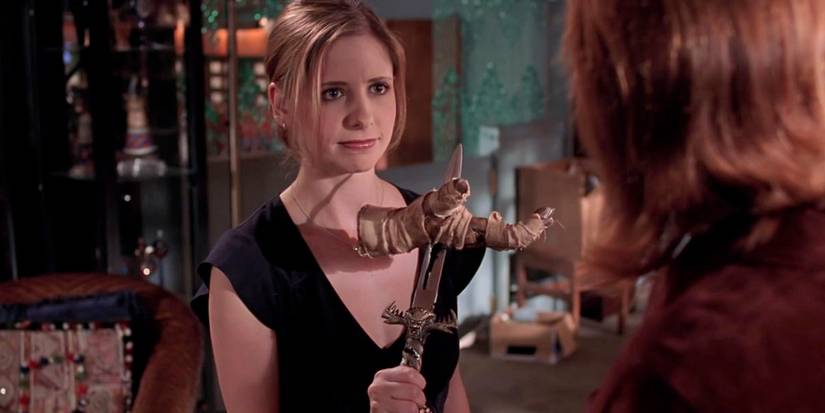 Sarah Michelle Gellar as Buffy with a mummy hand in Buffy the Vampire Slayer, looking concentrated.