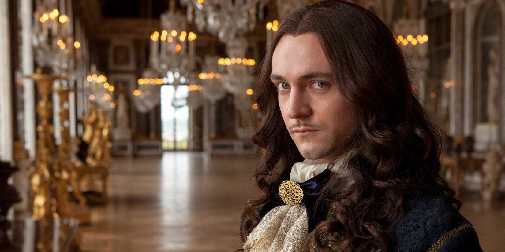 George Blagden as Louis XIV in 'Versailles' looking at the camera while standing in the hall of mirrors.