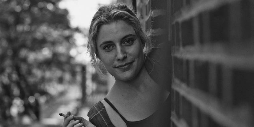 Greta Gerwig as Frances peeking out of a wall and looking at the camera in Frances-Ha.