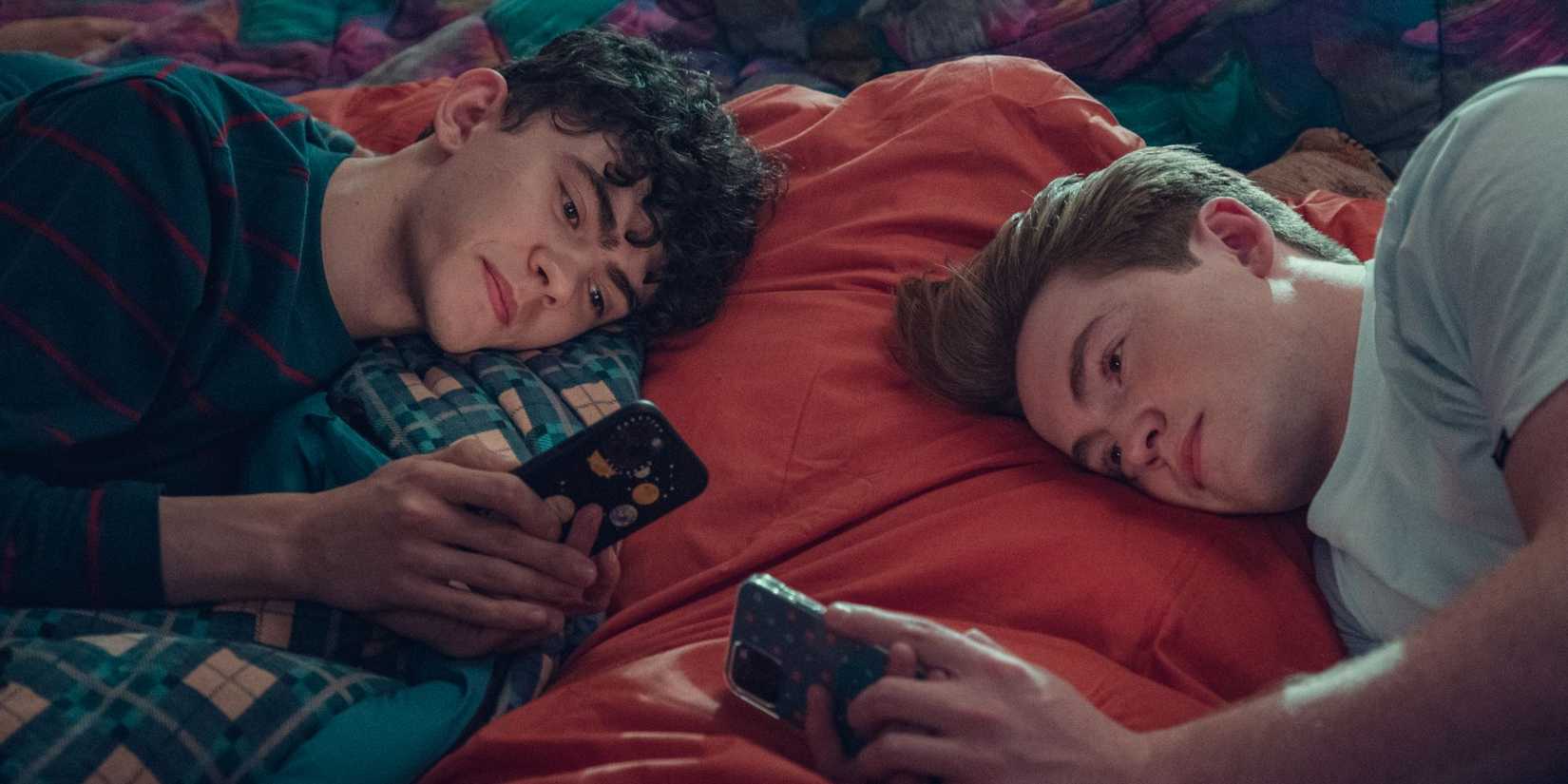 Charlie and Nick laying on their sides looking at their phones in Heartstopper Season 2