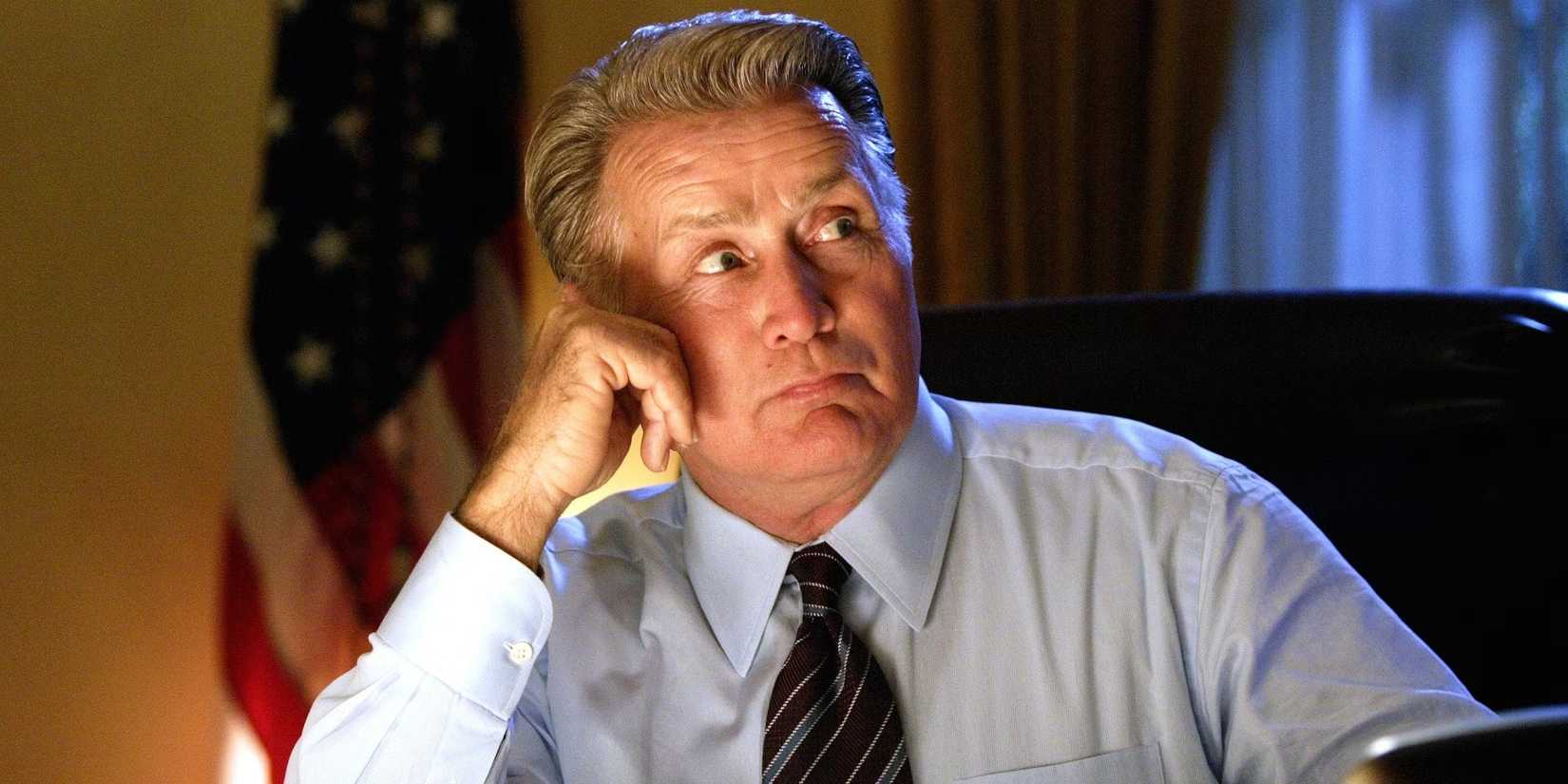 Martin Sheen sitting at a desk with an American flag behind in The West Wing.
