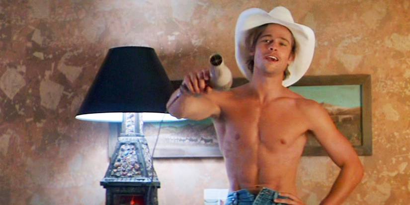 J.D., standing in a hotel wearing a cowboy hat and wielding a hair dryer like a handgun in Thelma & Louise