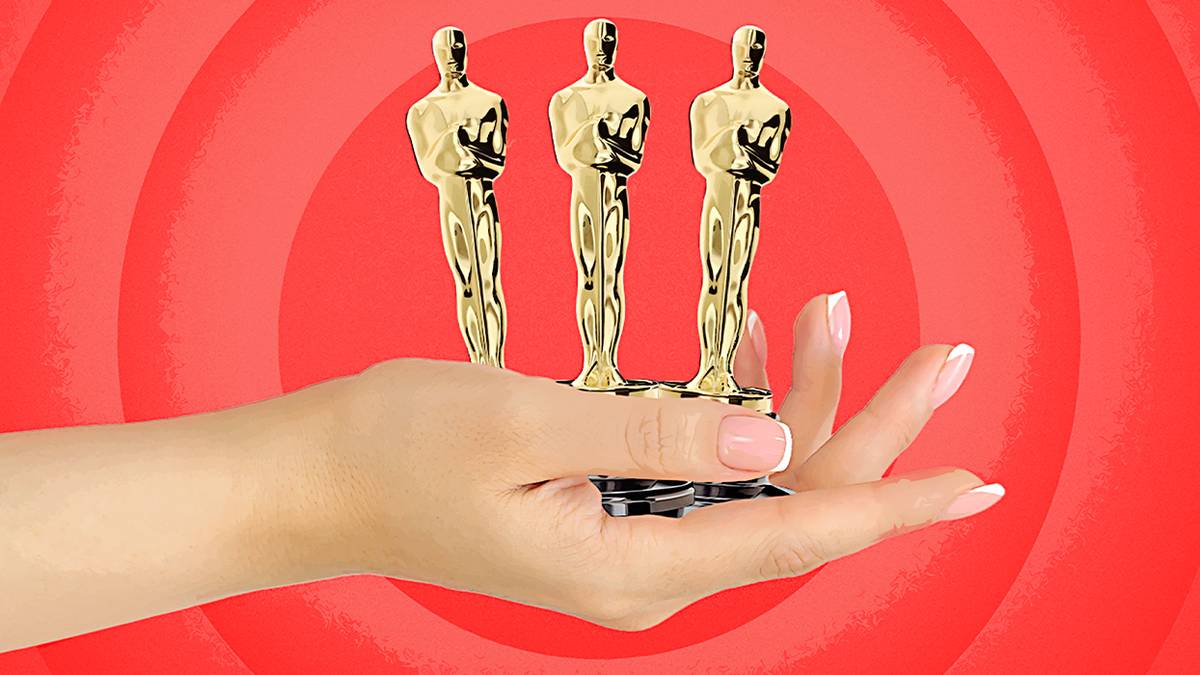 A hand holding three Oscar statuettes on a red background