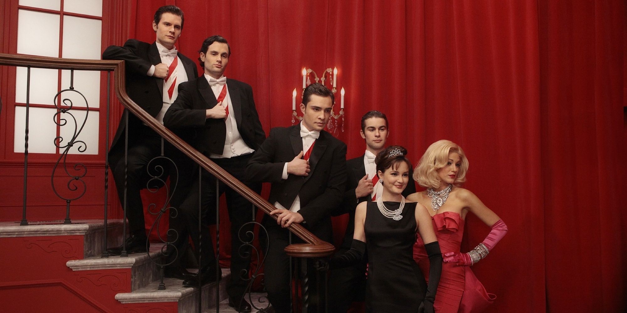 Gossip Girl cast dressed in formal wear and posing for a picture on a staircase in front of a red curtain