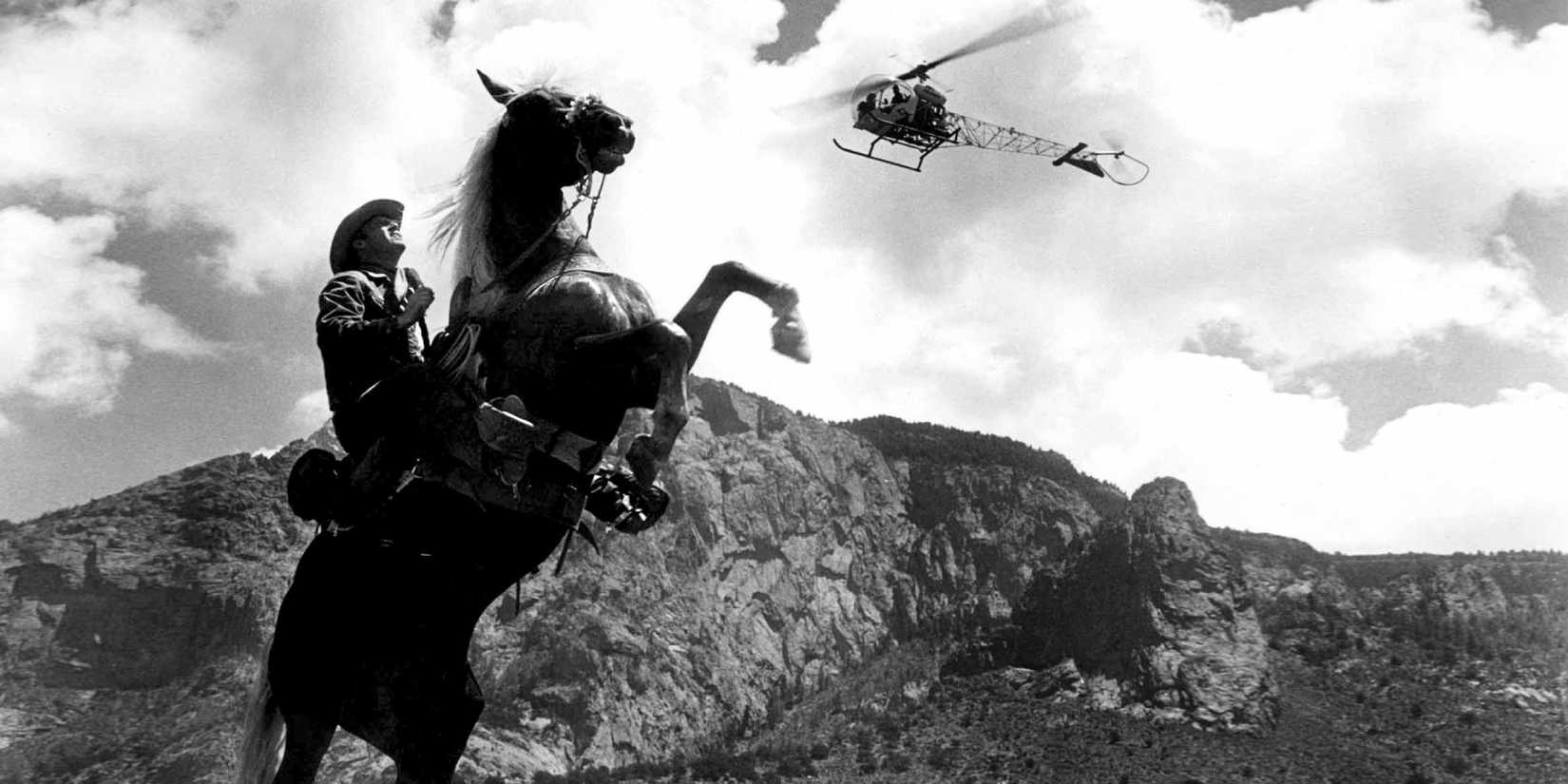 A cowboy on a horse in a rearing position with a mountain background and a helicopter flying overhead in Lonely Are the Brave