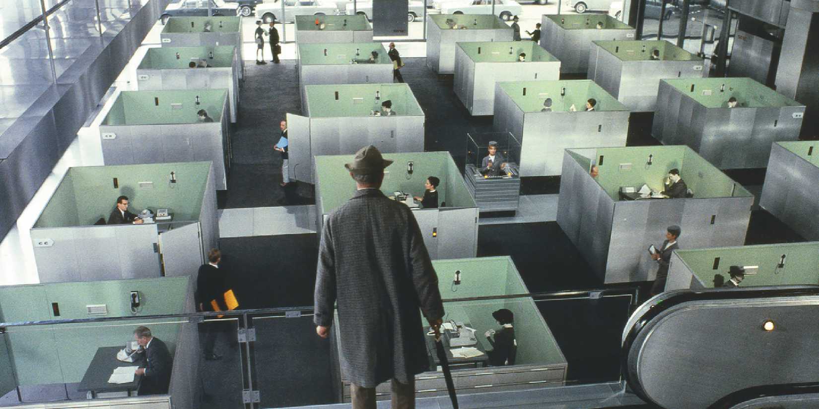 A man looking at a group of employees in cubicules in Playtime
