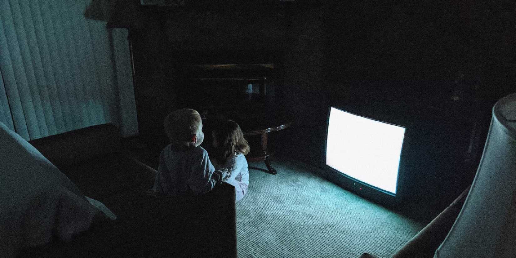 A child sitting in front of a staticky television in a dark room in Skinamarink