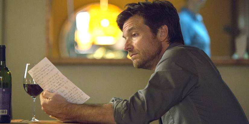 Jason Bateman reads a note while holding a glass of wine in The Gift.