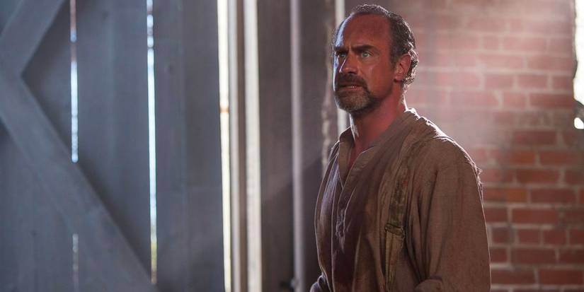 A bounty hunting slave catcher stands in a brick barn with sunlight streaming over him.
