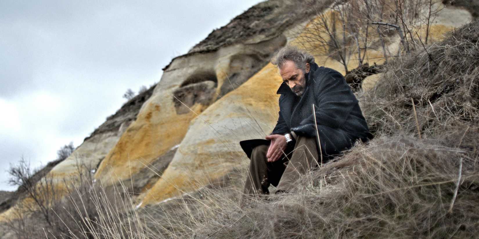 Aydin on a mountain covered in a blanket and looking pensive in 'Winter Sleep'