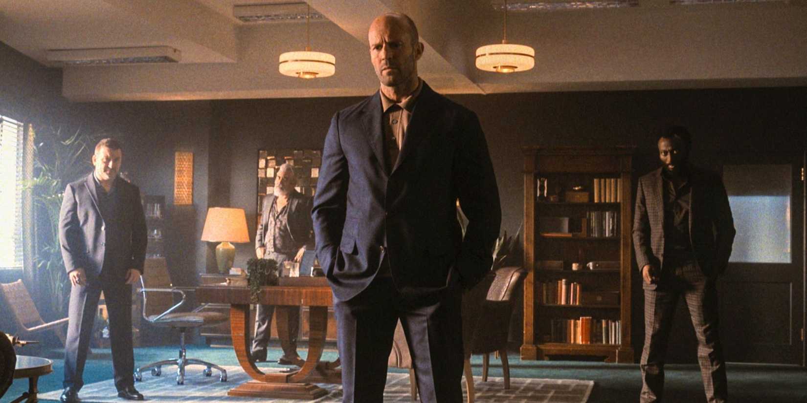 Mason Hargreaves standing with his hands on his pockets in a room with other men in Wrath of Man’ (2021) 