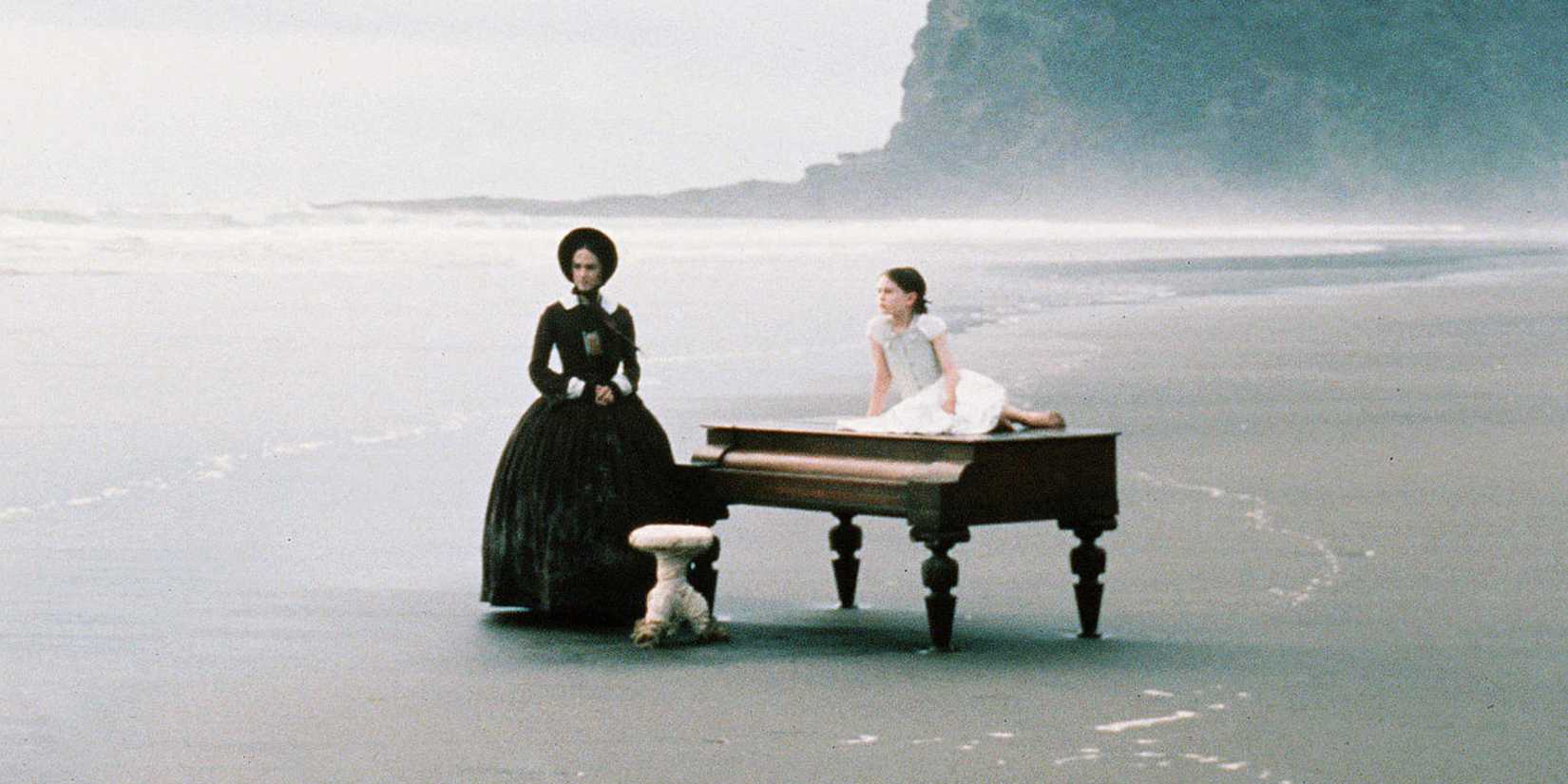 A shot of Anna Paquin and Holly Hunter standing in the middle of a beach with a black piano in The Piano