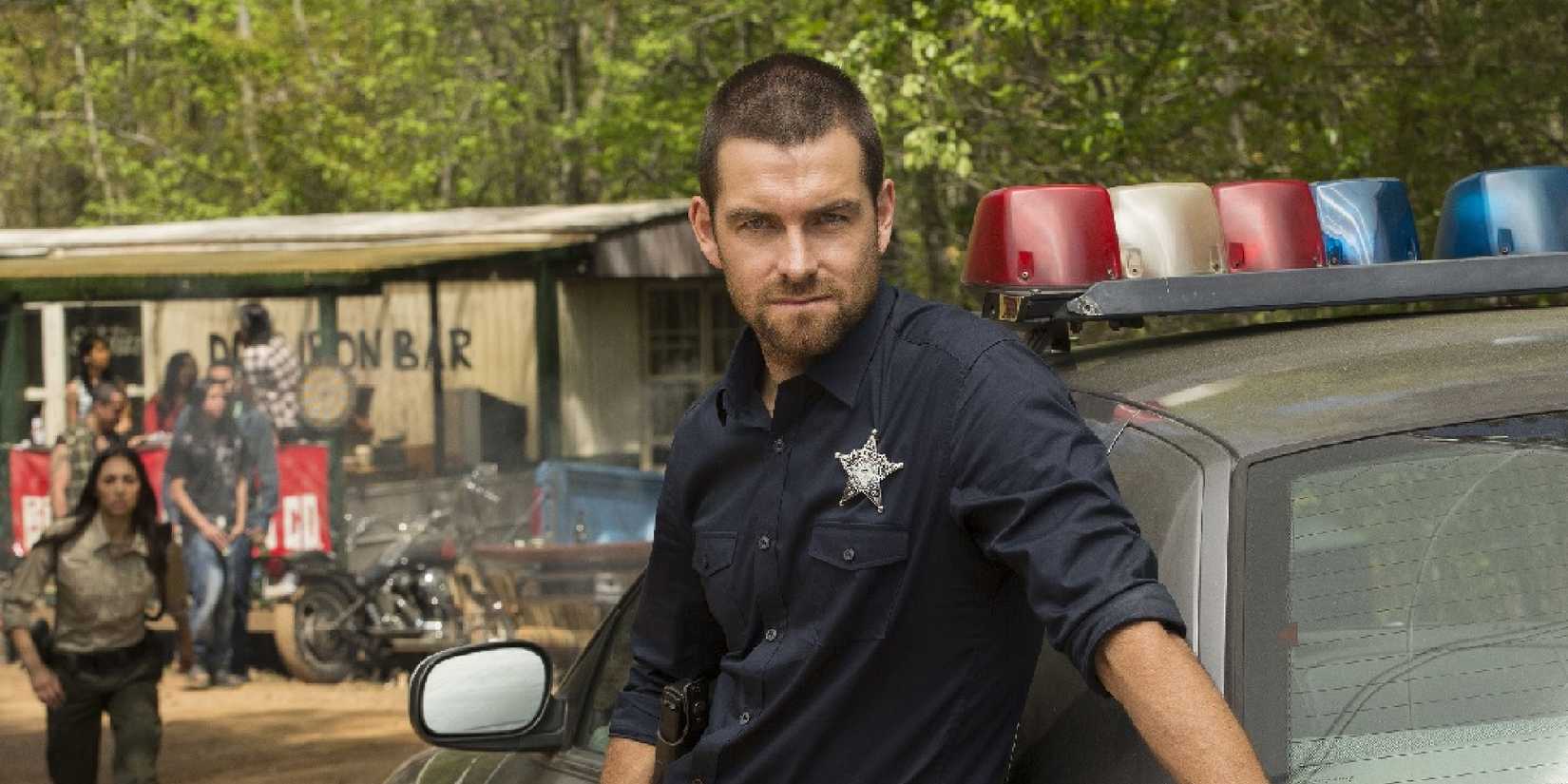 Antony Starr outside a shanty bar by a police car with a sheriff star on his shirt in Banshee.