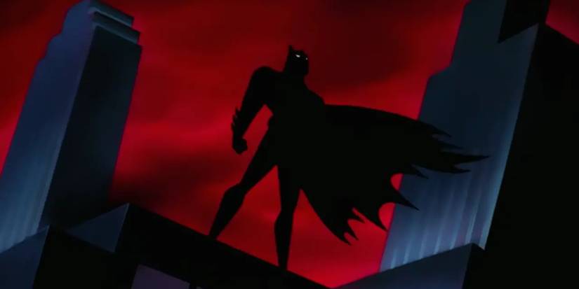 Batman's shadow standing atop a rooftop in front of buildings in Batman The Animated Series.