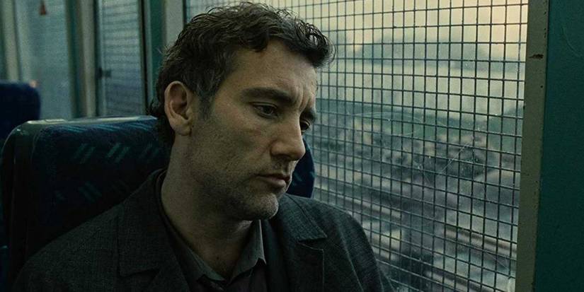 Clive Owen as Theo Faron sitting on a bus with barred windows in Children of Men.