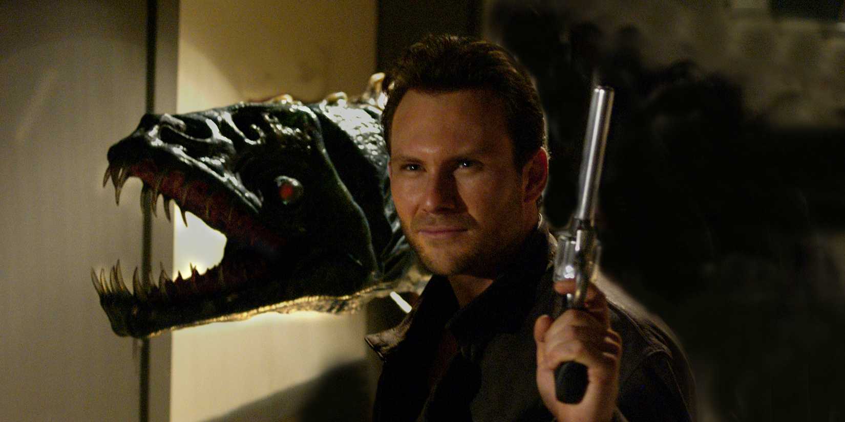 Christian Slater dans Alone in the Dark tenant un pistolet et souriant