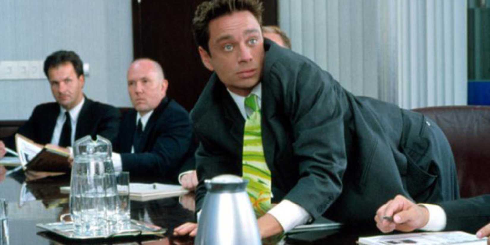 Chris Kattan as Corky Romano leaning on a conference table in Corky Romano