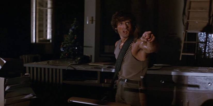 An armed John Rambo (Sylvester Stallone) points and yells at someone offscreen in First Blood (1982)