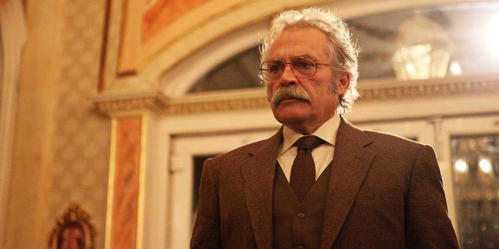 Haluk Bilginer in 'Sahsiyet' standing in front of a door wearing a brown suit