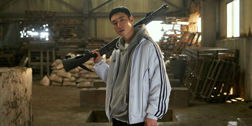 Lee Je Hoon holds a long gun over his shoulder in a warehouse in Time to Hunt.