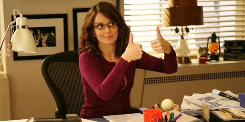Tina Fey as Liz Lemon giving two thumbs up in her office in 30 Rock.