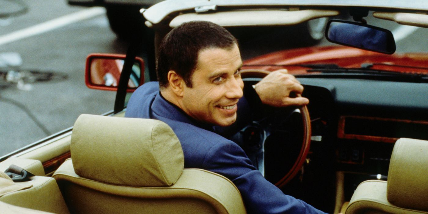 Russ (John Travolta) turning and smiling at someone as he drives a convertible in Lucky Numbers