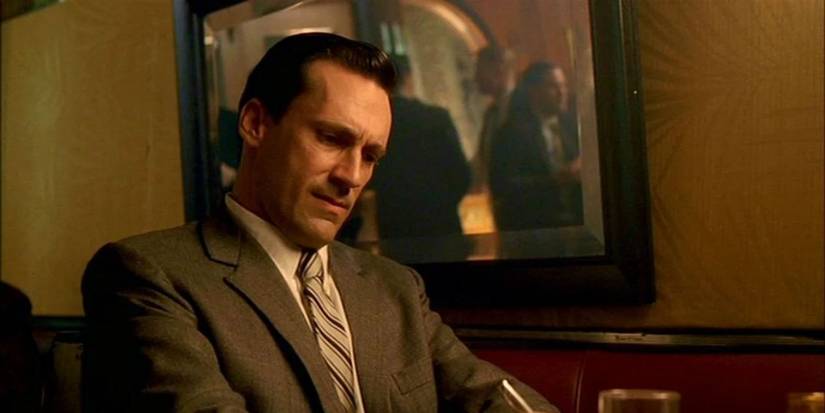 Don Draper sitting at his desk writing something and looking troubled in a scene from Mad Men.