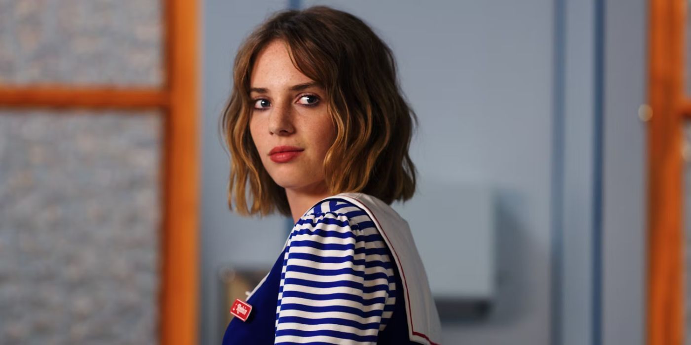 Maya Hawke as Robin in Stranger Things in a work uniform looking over her shoulder in Season 3.