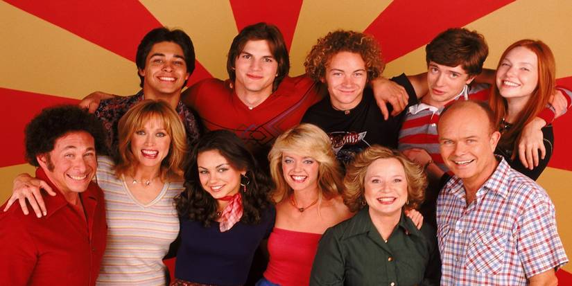 The cast of That 70s show gather together and pose in front of a yellow and red retro striped background.