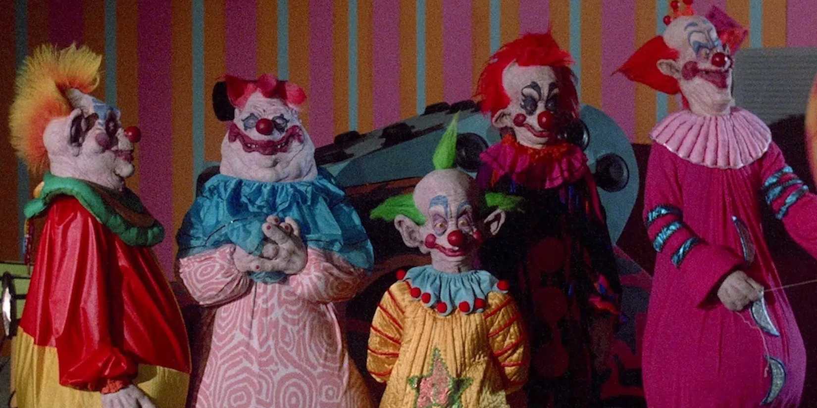 The clowns from 'Killer Klowns from Outer Space' standing against a multi-colored wall.
