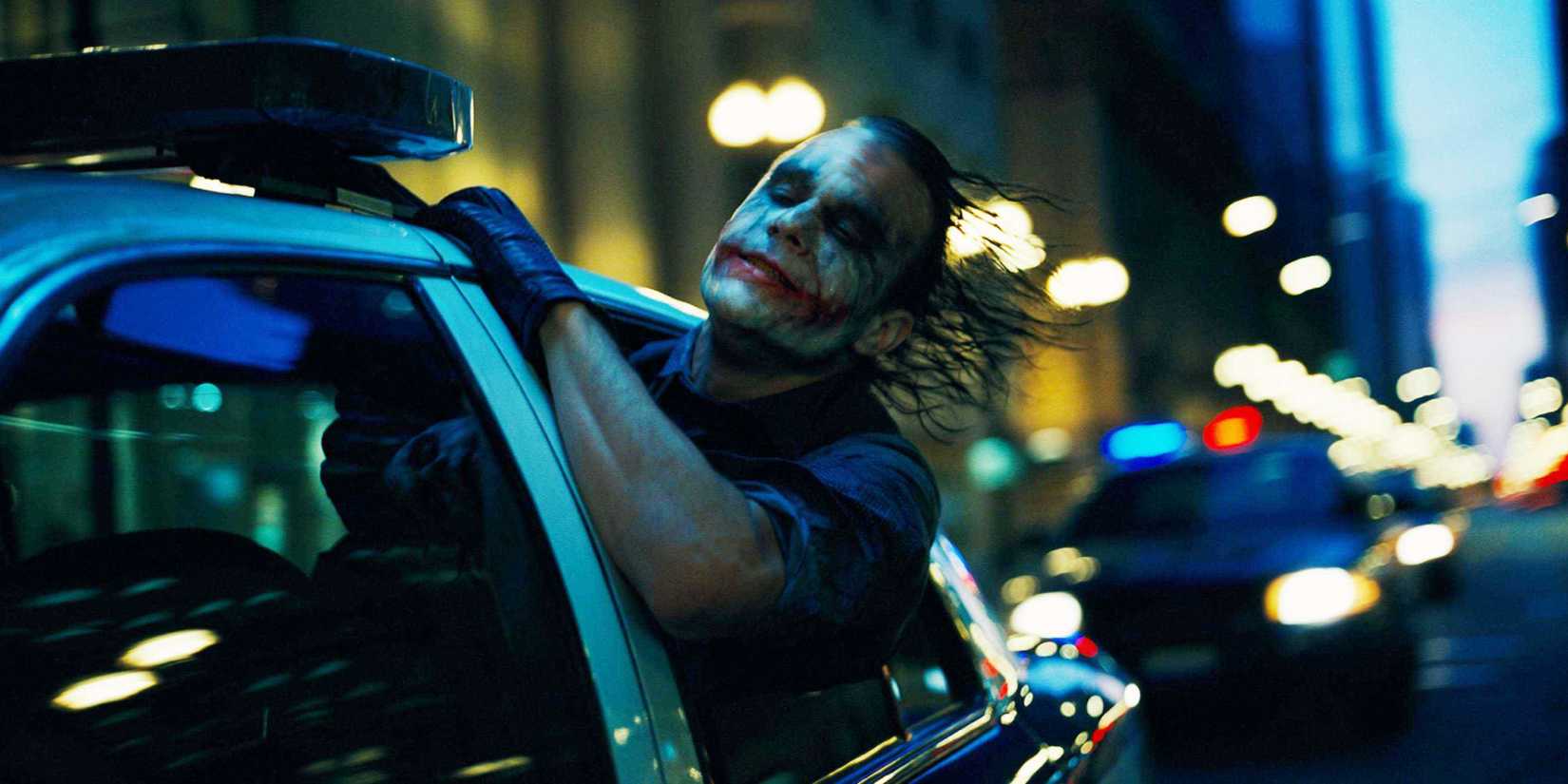 Heath Ledger sebagai Joker menjulurkan kepalanya ke luar jendela mobil yang melaju di jalanan di The Dark Knight.