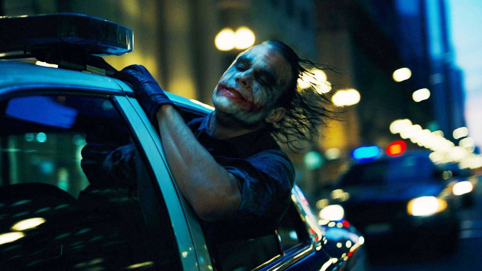 Heath Ledger as The Joker sticks his head out the window of a car racing down the streets in The Dark Knight.