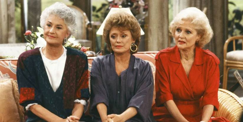 Bea Arthur as Dorothy, Rue McClanahan as Blanche & Betty White as Rose sitting on a couch in The Golden Girls.