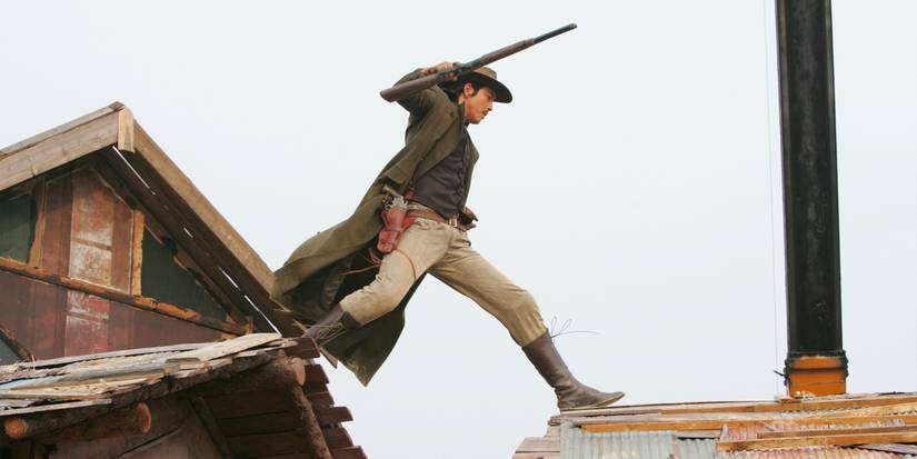 Jung Woo-sung walking across a rooftop and holding a rifle in The Good, the Bad, the Weird