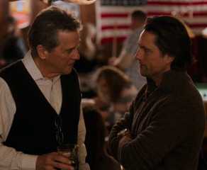 Doc and Jack talk in a tavern with other people in the background in Virgin River.