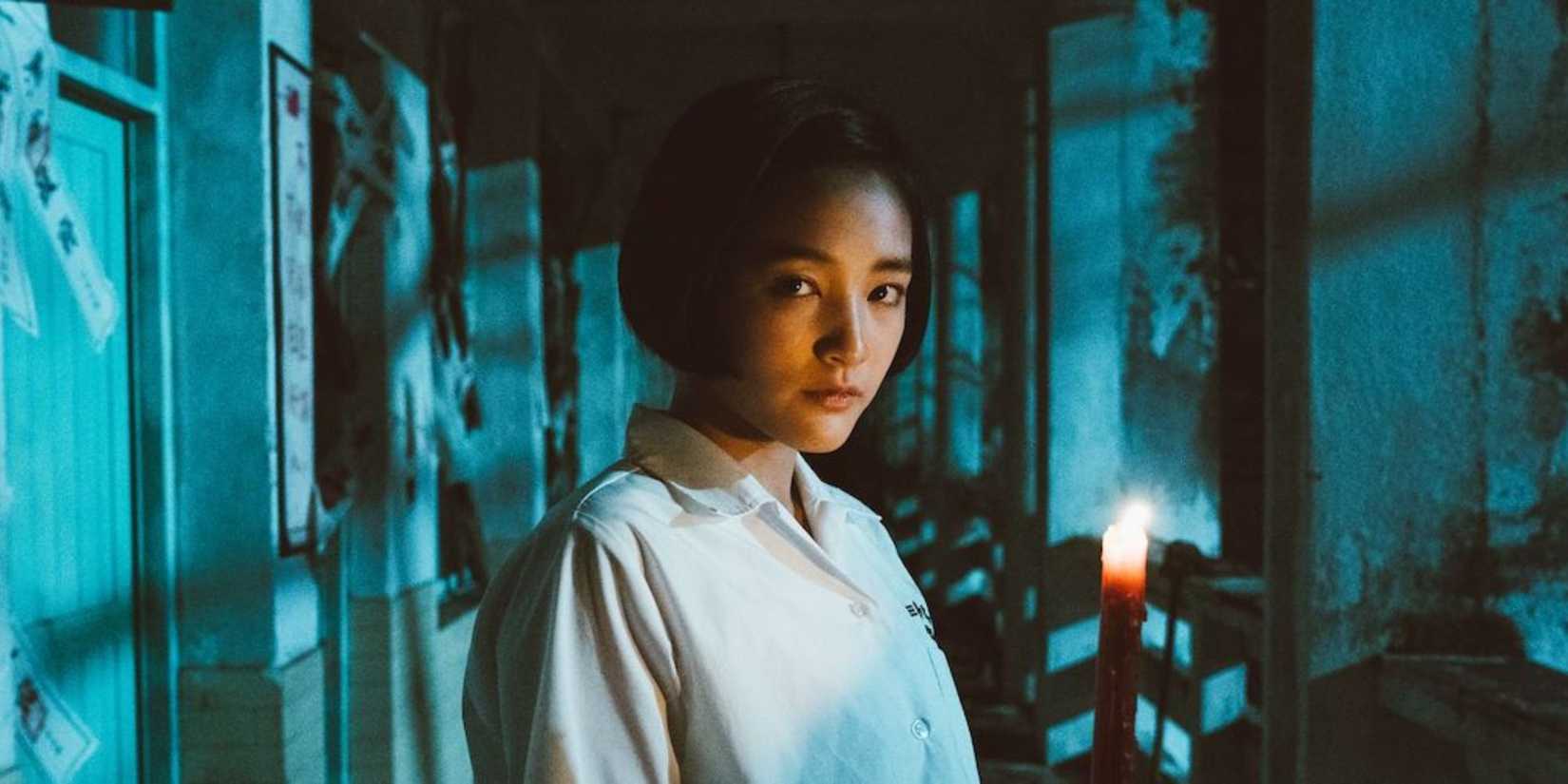 Seorang wanita berdiri di lorong sambil memegang lilin