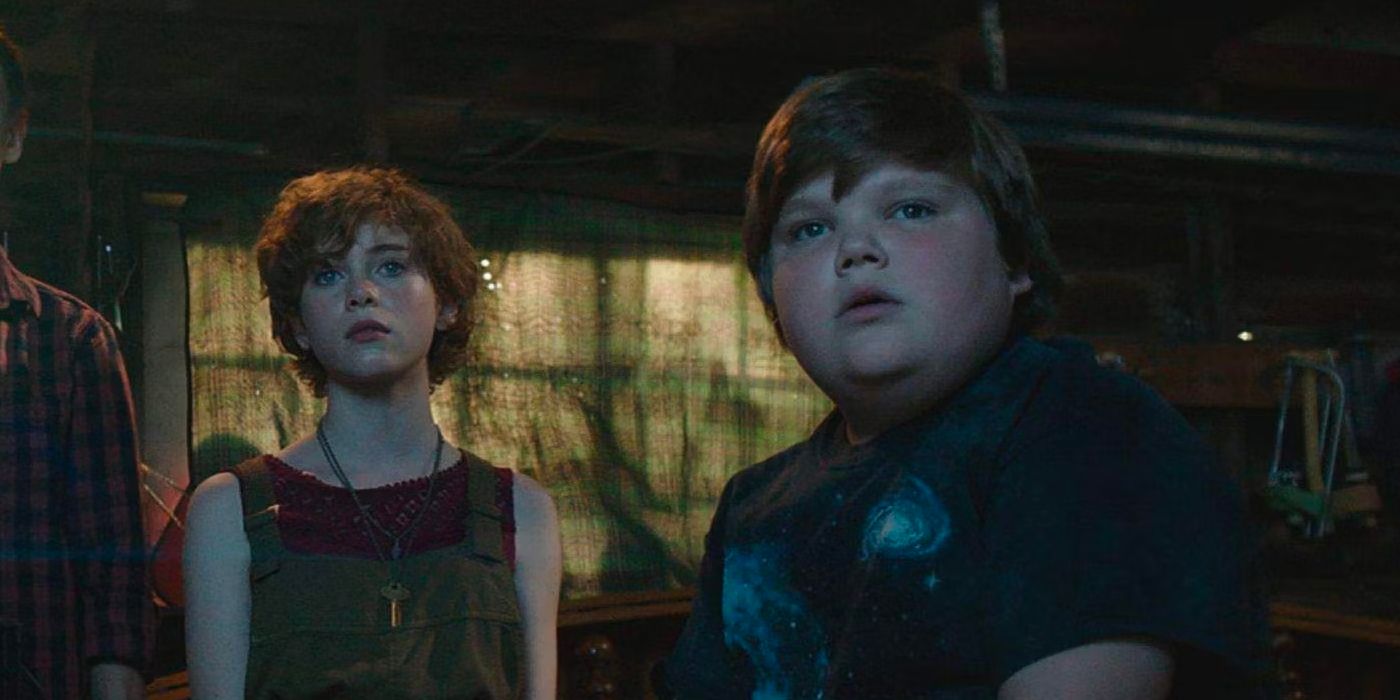 Sophia Lillis and Jeremy Ray Taylor in a dark room looking terrified as they gaze up at a screen in It (2017).
