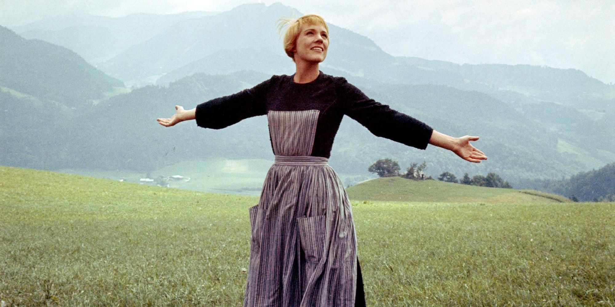 Maria standing in the field and smiling with open arms while looking at the sky in The Sound of Music.