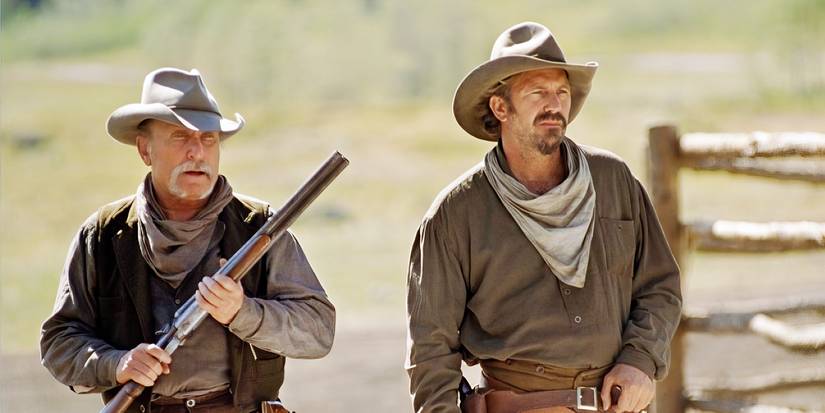 Charley Waite and Boss Spearman, standing outside while Boss holds a rifle in Open Range
