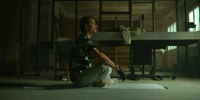 Michael Fassbender as The Killer sitting on the floor looking ahead in 'The Killer'.